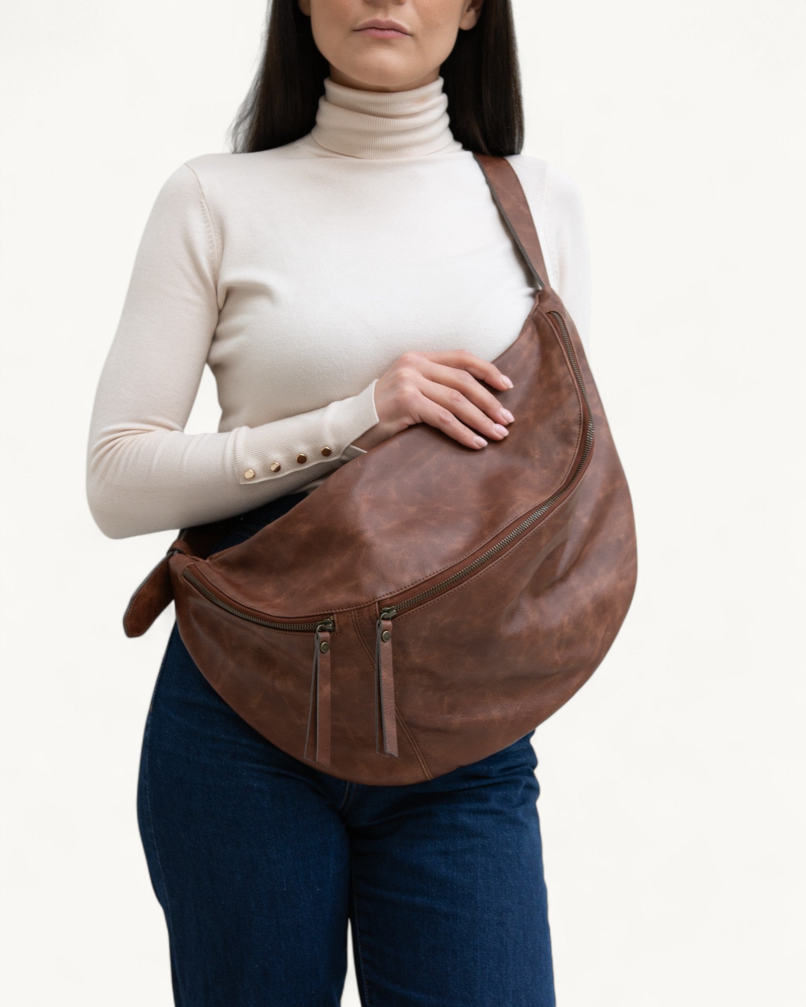 Person holding a brown leather fanny pack against a white background