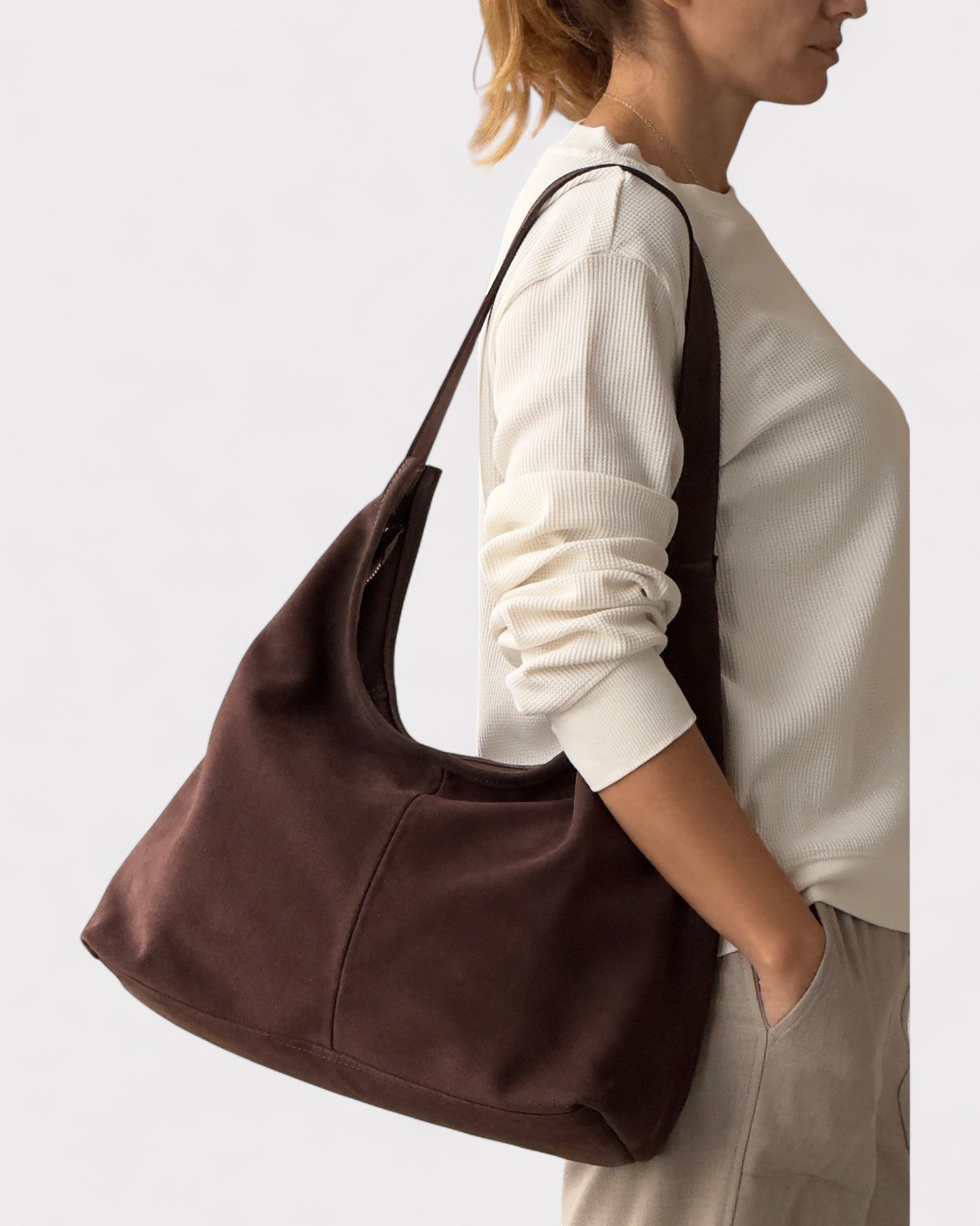 Person carrying a brown leather handbag on a plain background