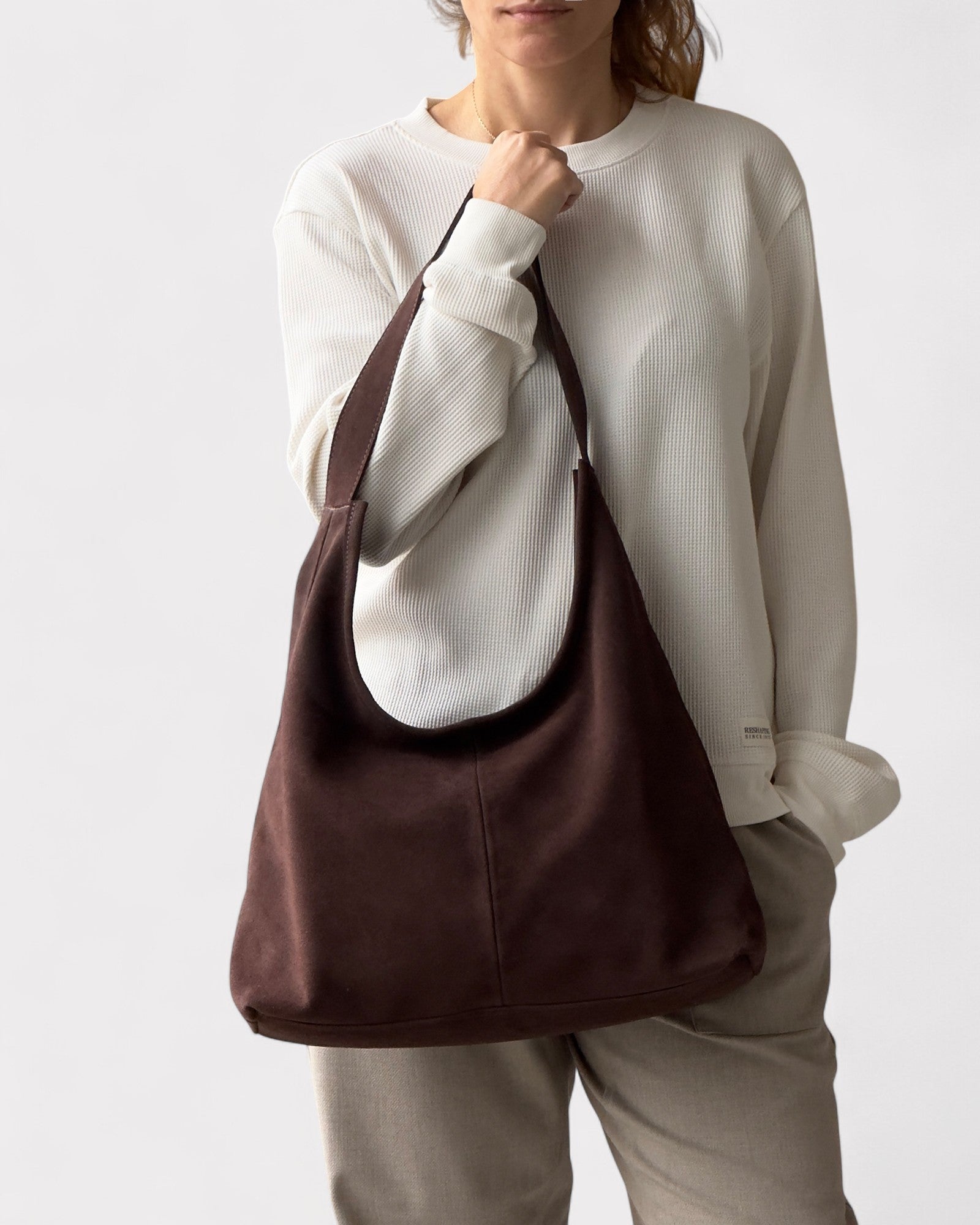 Person holding a brown shoulder bag against a white background