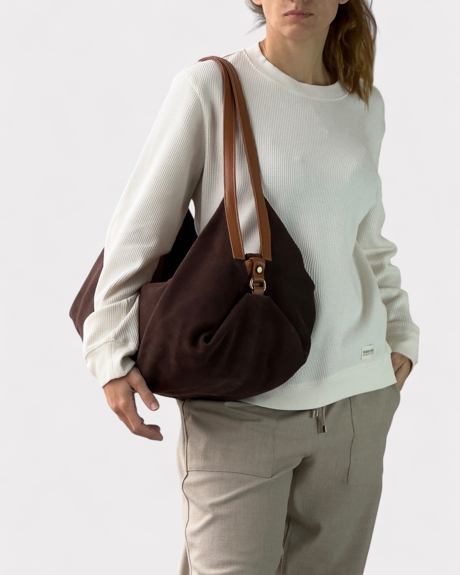 Person wearing a brown shoulder bag on a plain background