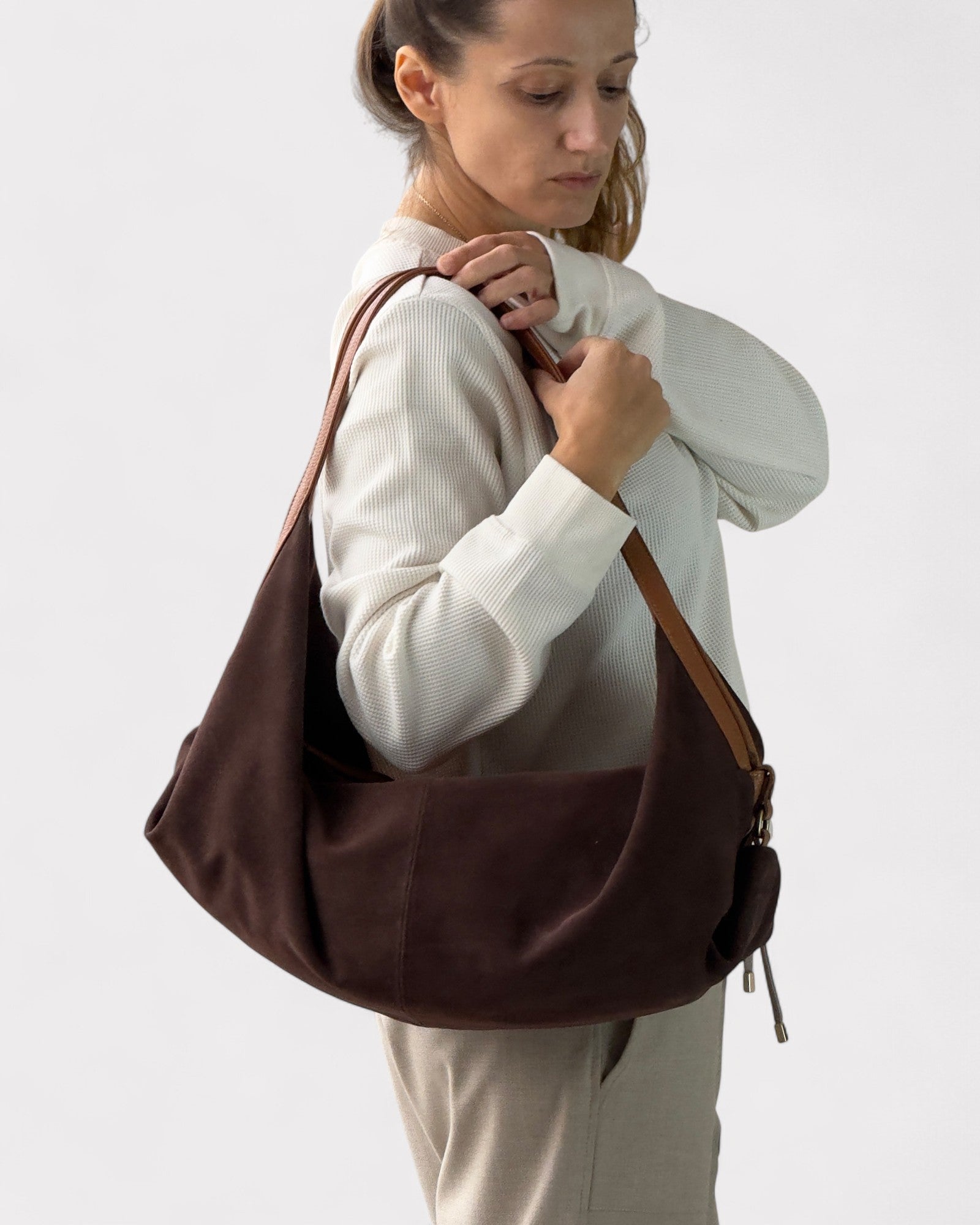 Woman holding a brown shoulder bag against a plain background