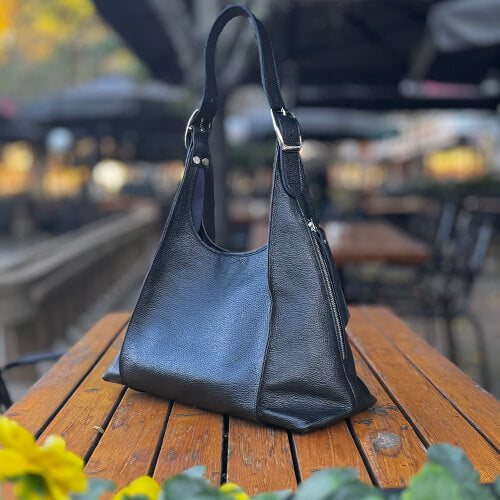 Black leather handbag on a wooden table with a blurred outdoor background