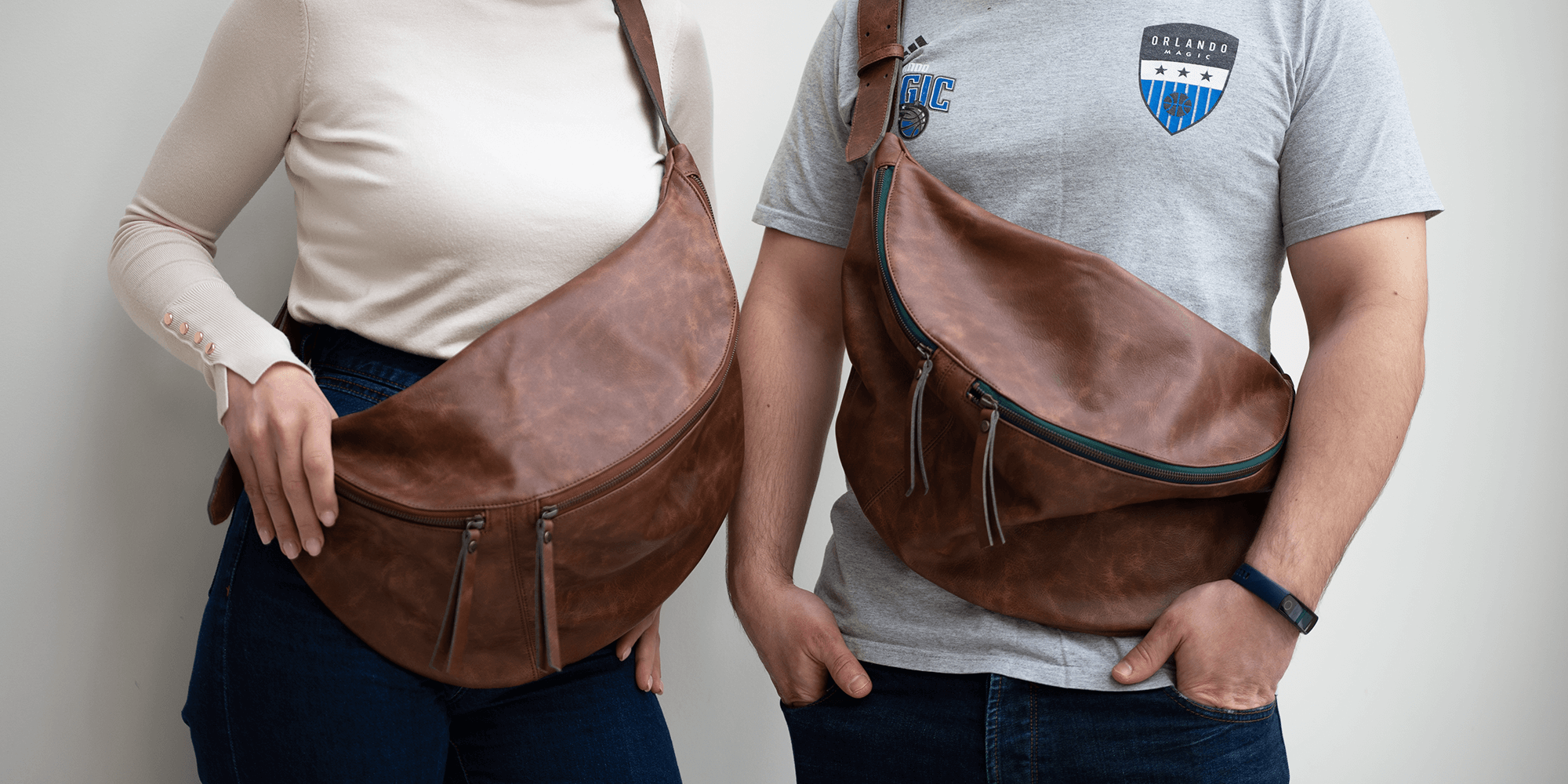 Two people wearing brown leather crossbody bags against a plain background